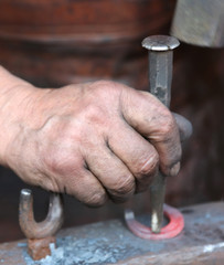 hand elder blacksmith who uses an iron awl over a anvil