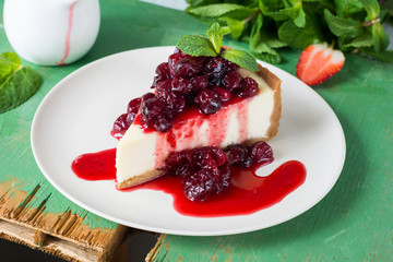 Slice of cheesecake with cranberry sauce decorated with mint leaf on a white plate