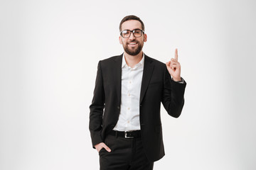 Handsome young bearded businessman wearing glasses pointing to copyspace.