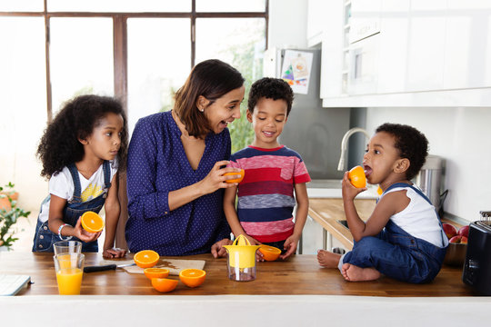 Une m&egrave;re et ses trois enfants pr&eacute;parent du jus d'orange dans la cuisine