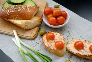 Top view of a crusty baguette slices with cherry tomatoes and green olives, cream cheese, healthy breakfast or snack on a wooden board
