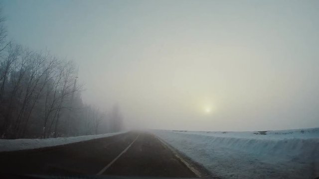 Driving car in winter in fog. The sun shines through the fog