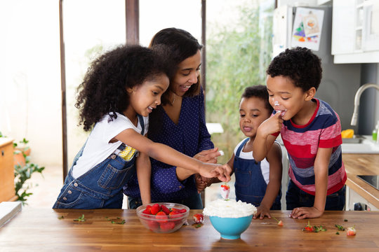 Une m&egrave;re et ses enfants mangent des fraises avec de la chantilly dans la cuisine