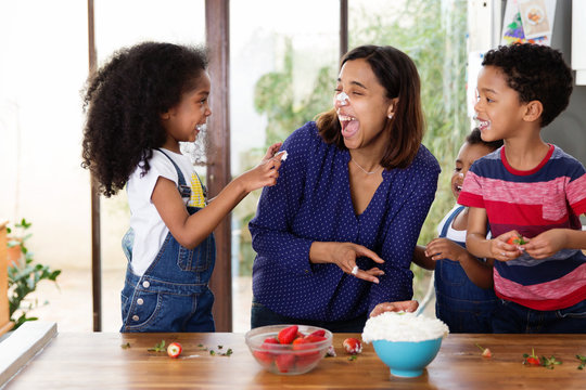 Une m&egrave;re et ses enfants jouent &agrave; se mettre de la chantilly sur le nez dans la cuisine