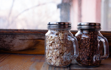 Glass jars with oatmeal and buckwheat on the wooden background