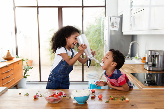 Une petite fille verse de la chantilly dans la bouche de son petit fr&egrave;re