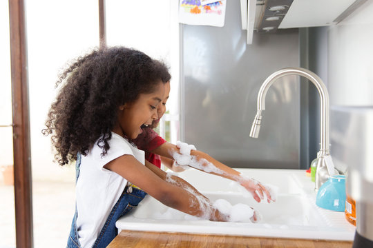 Deux enfants rient en faisant la vaisselle dans la cuisine