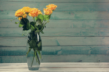 Bouquet of yellow roses in glass vase over
 old wooden background