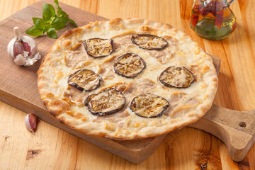 Pizza with eggplant, cheese and pork on a wooden cutting board.