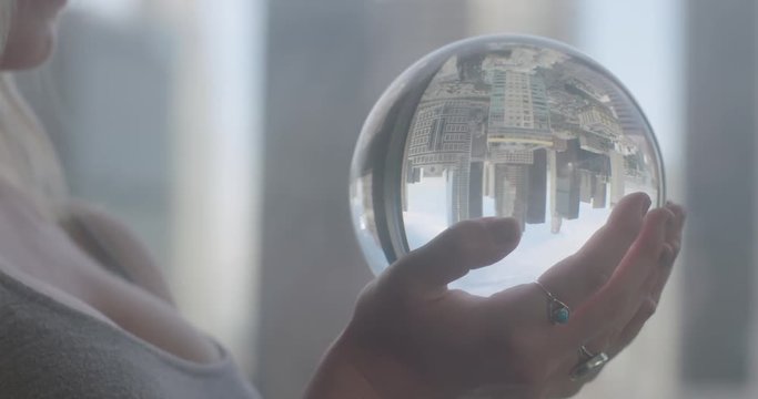 Young woman's hands holding crystal ball in an apartment window high above Downtown Los Angeles.  Close up, recorded with black Promist filter in slow motion at 60fps.