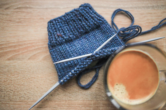 Knitting needles, blue yarn, black coffee are on the table. Wooden background. Hobbies 