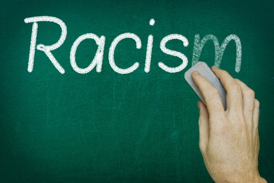 Hand erasing the word RACISM written on blackboard