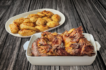 Plateful of Roasted Lamb Shoulder with Seasoned Potato Halves Set on Old Weathered Cracked Wooden Table Surface