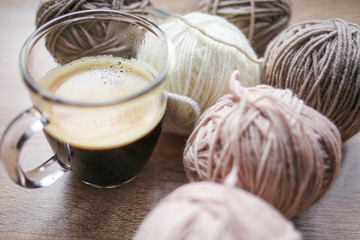 Coffee, knitting needles, beige and white yarn are on the table. Wooden background. Hobbies 