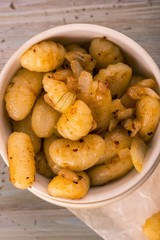 Top view on portion of fried gnocchi with onion in light bowl