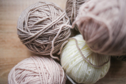 Knitting needles, beige and white yarn are on the table. Wooden background. Hobbies 