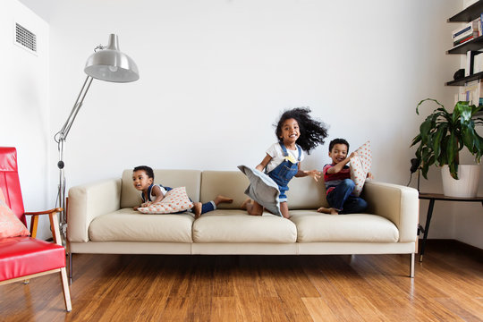 Trois enfants jouent avec des coussins sur le canapé du salon