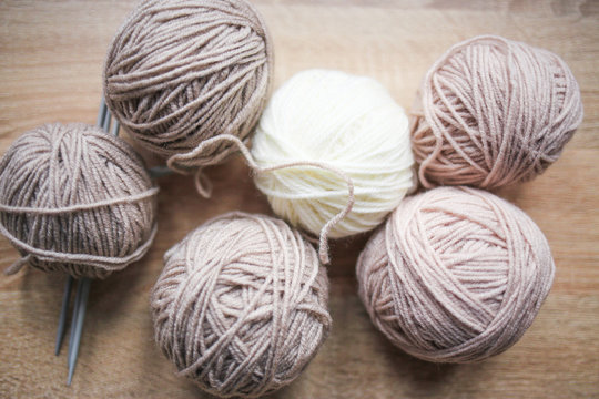 Knitting needles, beige and white yarn are on the table. Wooden background. Hobbies 