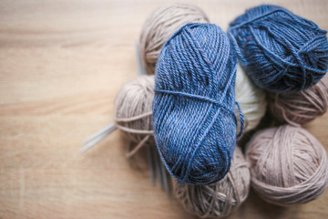 Knitting needles, beige, white and blue yarn are on the table. Wooden background. Hobbies 