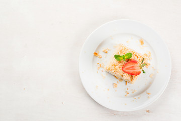 Light dessert: a classic Napoleon or millefeuille cake decorated with mint and strawberries. On a white plate, on a white wooden table. 