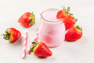 Summer dessert or breakfast - strawberry milkshake with mint, in a small jar, with a striped tube. On a white table. copy space