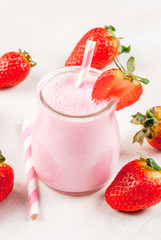 Summer dessert or breakfast - strawberry milkshake with mint, in a small jar, with a striped tube. On a white table. copy space
