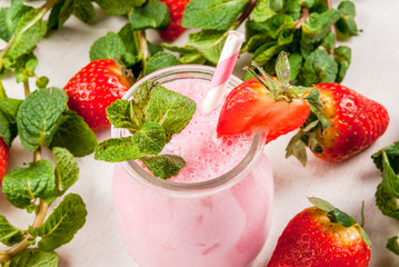Summer dessert or breakfast - strawberry milkshake with mint, in a small jar, with a striped tube. On a white table. copy space