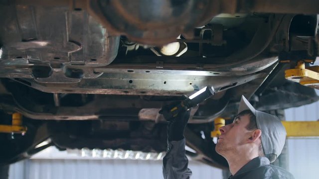 Mechanic is checking the bottom of car in garage automobile service, close up