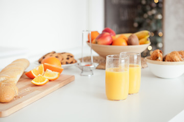 Plate of tasty cookies with chocolate crumbs, croissant, baget, bananas, apples, persimmon, orange and orange juice on white table