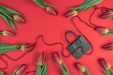 Gift, sale, shopping concept. Tulips composition with paper shopping bag on red background. Flat lay, top view.
