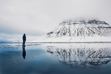 Man standing on an icy lake in front of a mountain engulfed in clouds 