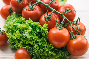 Macro photo of ripe tomatoes and green lettuce on a wooden table. Tomatoes on a branch