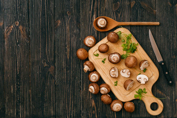 Royal Champignons with greens on wooden cutting board with kitchen knife on black rustic background, top view. Vegan or vegetarian healthy food concept.