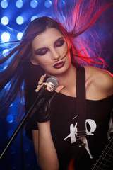 Beautiful girl with a microphone and a guitar in hand on stage singing a song in rock style, closeup