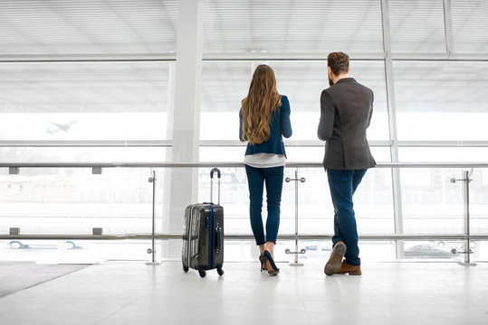 Business couple standing together with baggage near the window at the departure area at the airport