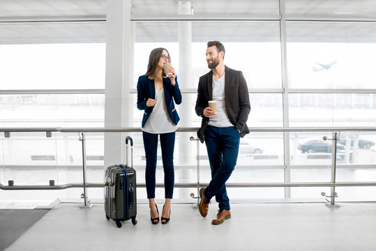 Business couple standing together with baggage and coffee cups near the window at the departure area at the airport