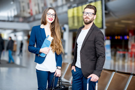 Elegant business couple standing with suitcase and airplane tickets at the waiting hall in the airport. Business travel concept
