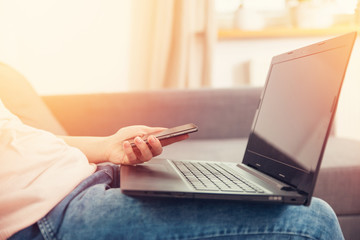 Close-up of female hands using smart phone while working on computer at home, flare light