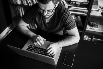 Man worn glasses. Software Engineer is sitting and working. He is looking into his laptop. Black and white photo.
