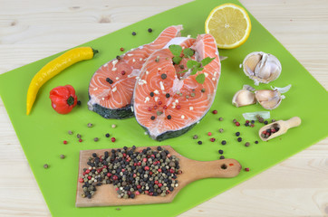 Fresh and juicy salmon steaks surrounded with spices, lemon and garlic on green kitchen mat
