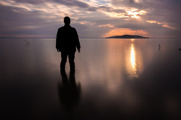 Long exposure shot of a silhouette of a man in water in front of a sunset - Powered by Adobe