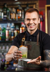 Cheerful bartender gives the cocktail to customer.