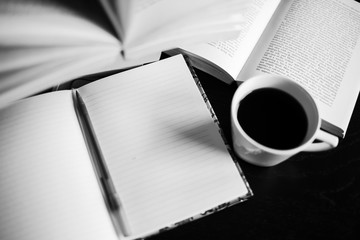 There are coffee, books, notebook and pen. Note-taking. Black and white photo