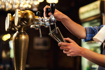 Bartender pouring the fresh beer in pub,barman hand at beer tap pouring a draught lager beer,beer from the tap,Filling glass with beer,fresh beer,pub.Bar.Restaurant.European bar.American bar.