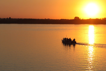 Boat with people on a sunset background floating on the river