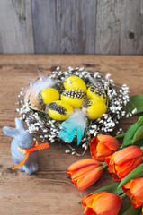 Nest with Easter eggs and a cute little Easter rabbit. Delightful orange tulips on a brown wooden background.