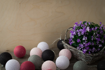 Grey wicker basket with beautiful purple flowers. Multicolored garland in the form of balls, which wrapped in thread.