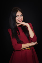 Obraz premium A beautiful woman with black straight hair and blue eyes in a burgundy dress on a dark background. Close-up. Space for text