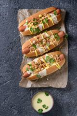 Hot dogs with sausage, fried onion, coriander leaves, cheese sauce and mustard, served on baking paper over black concrete texture background. Fast food. Top view, copy space