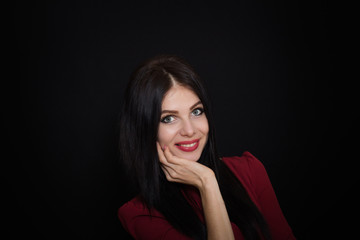 Fototapeta premium A beautiful woman with black straight hair and blue eyes in a burgundy dress on a dark background. Close-up. Space for text